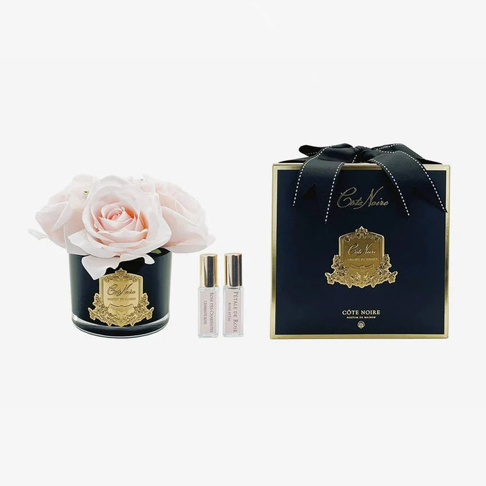 a bouquet of pink roses in a black vase, a small black box with gold accents, and two small bottles of perfume.
