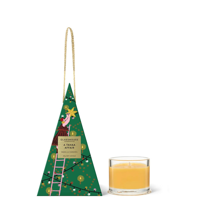 A green triangular box with a Christmas tree design and a gold handle, next to a small glass candle holder with a lit candle inside.