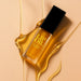A bottle of LIP OIL, specifically the Citrusburst product, is shown with a golden liquid dripping from it against a peach-colored background.