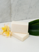two rectangular bars of white soap with the word "Koh Living" printed on them, placed on a white surface next to a yellow flower and a green leaf.