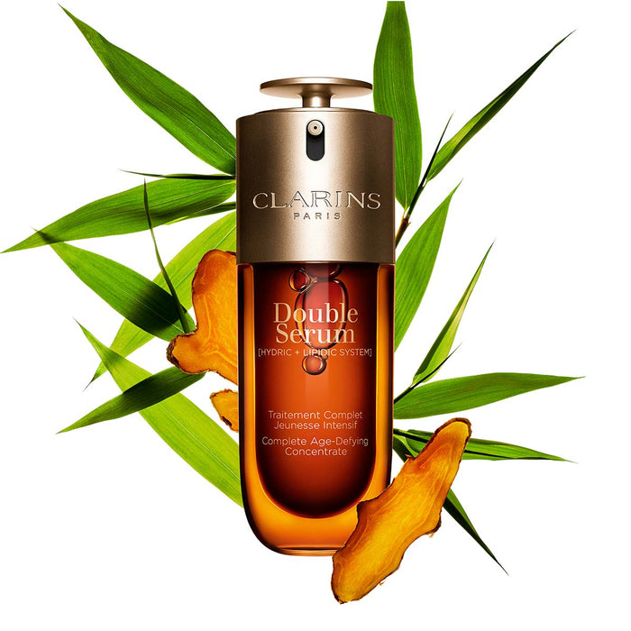 a bottle of Clarins Double Serum Hydericlic-Topical System, surrounded by green leaves and orange pieces.