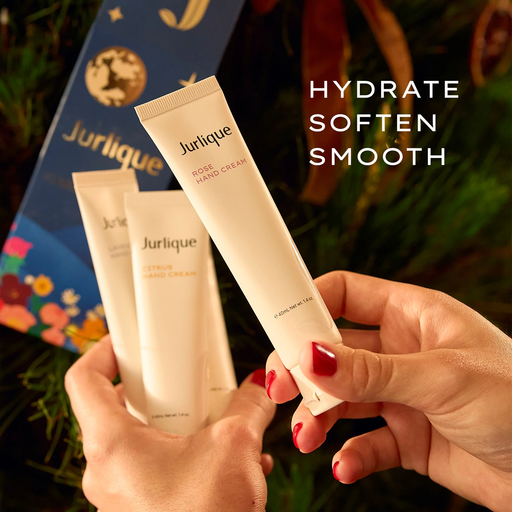 A person's hands holding two tubes of Jurique hand cream, with a background of a Christmas tree and a blue gift box.