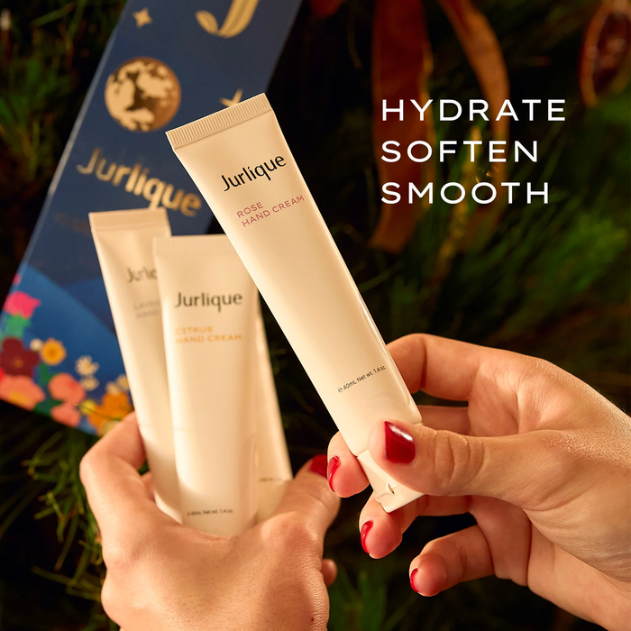 A person's hands holding two tubes of Jurique hand cream, with a background of a Christmas tree and a blue gift box.
