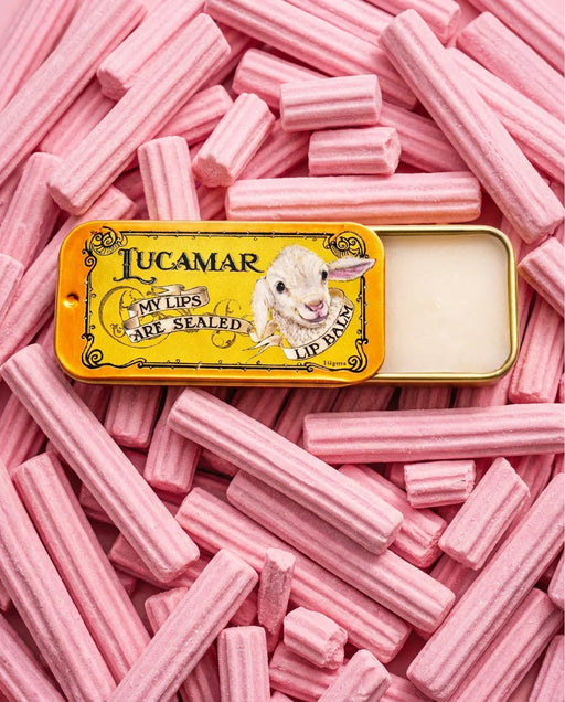A tin of pink lip balm with a picture of a lamb on it, surrounded by pink lip balm sticks.