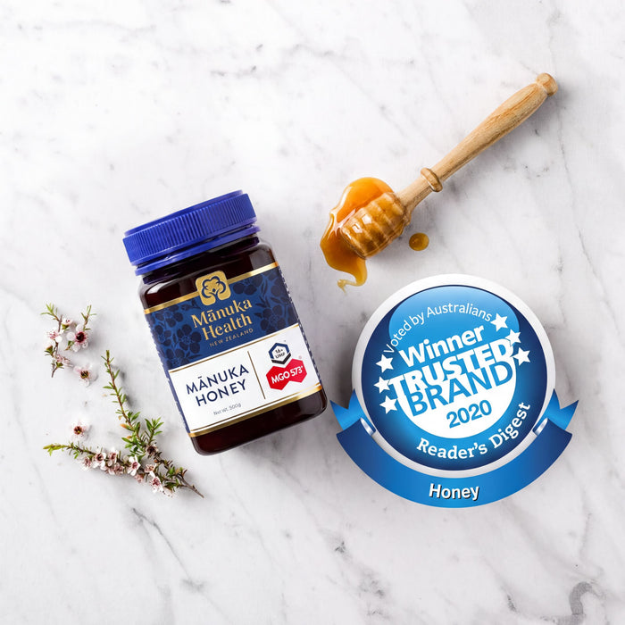 a jar of Manuka Honey, a honey jar, and a honey dipper on a marble surface.