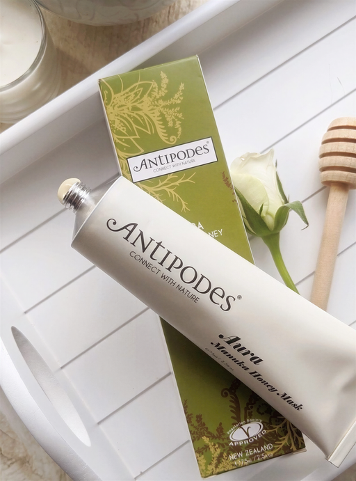a tube of Antipodes' Honey Mask and a box of the product, along with a honey dipper and a white rose.