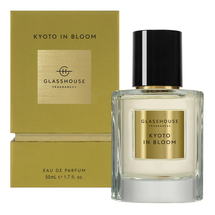 a bottle of Glasshouse Fragrance's Kyoto in Bloom eau de parfum, which is a 50ml eau containing 1.7 fluid ounces. The bottle is placed next to its packaging, which is a gold-colored box with the text "KYOTO IN BLOOM" and "GLASSHOUSE Fragrance" printed on it.