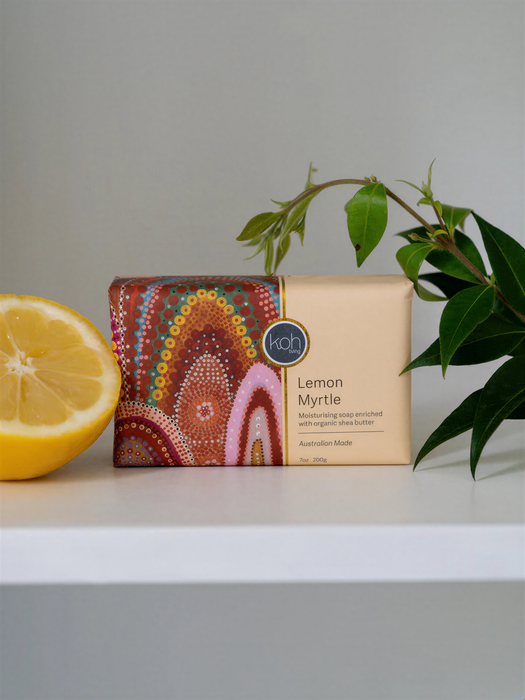 A bar of soap with a colorful, patterned design sits on a white surface next to a lemon slice and a green plant.