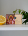 A bar of soap with a colorful, patterned design sits on a white surface next to a lemon slice and a green plant.