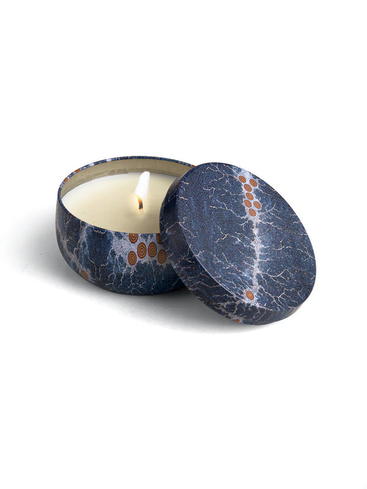 A blue and white patterned tin candle holder with a lit candle inside, placed on a white surface.