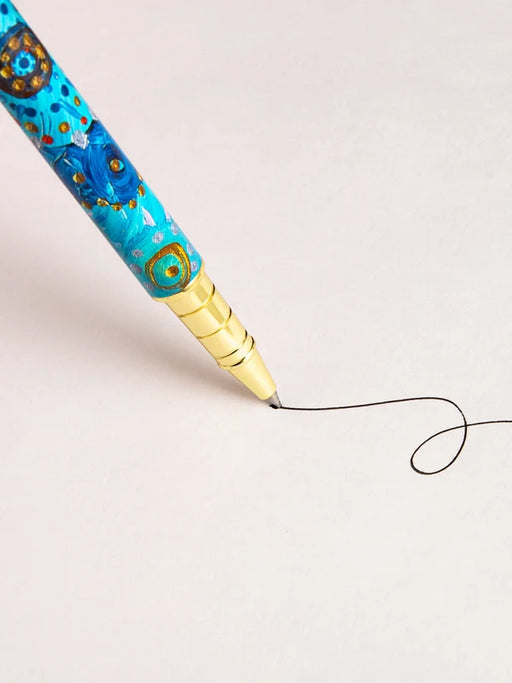 A close-up view of a pen with a colorful, patterned design on its body, with a black ink line being drawn on a plain white background.