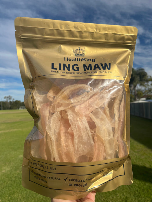 A hand holding a bag of dried fish, specifically Chinese dried fish, against a backdrop of a blue sky and green grass.