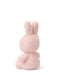 A pink stuffed bunny toy is sitting on its back with its ears perked up, facing away from the camera.