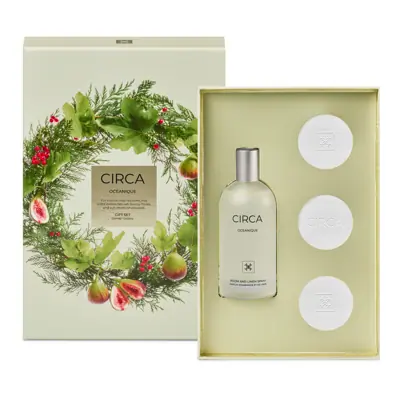 a gift set with a bottle of CIRCA Cosmetics and three white circular items, all presented in a white box with a wreath design.