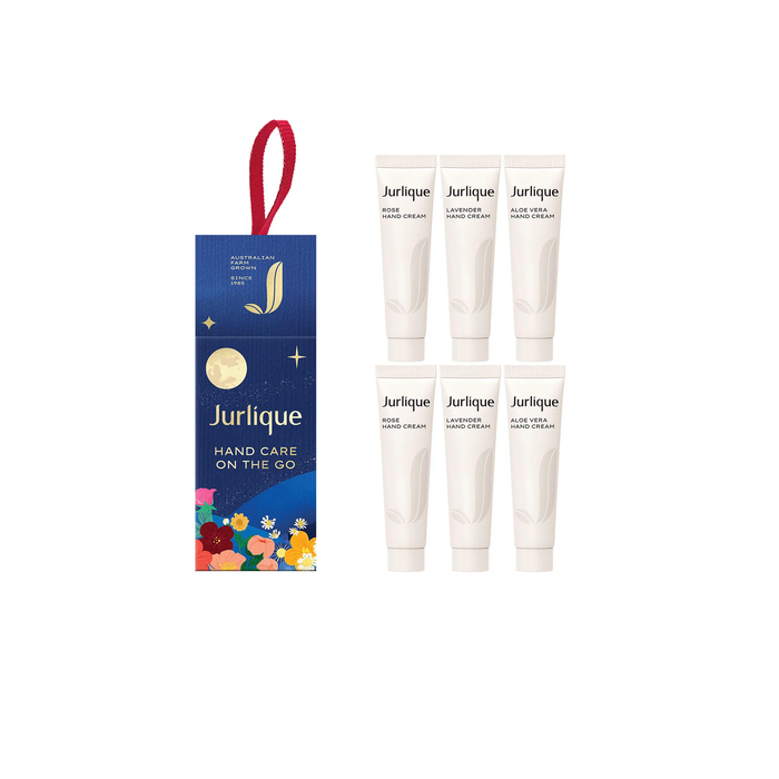 a set of six tubes of Jurlique hand care products, each with a different scent, arranged in a row. The tubes are white and have a red ribbon attached to them. The packaging for the products is blue and features a floral design.