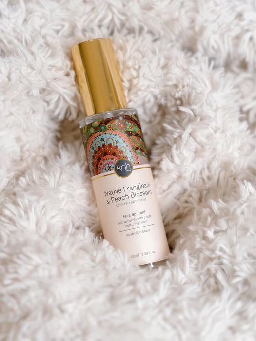 A bottle of "Native Frangipani & Peach Blossom" perfume with a gold cap, placed on a fluffy white surface.