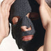 A close-up of a person's face wearing a black hexagonal patterned mask, with their hands covering their face.