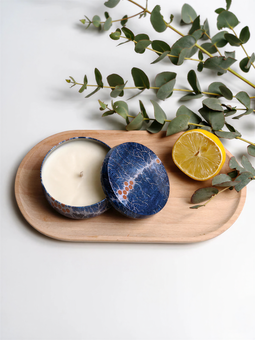 a wooden tray with a candle in a blue tin, a lemon slice, and some greenery.