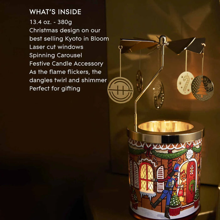 A decorative Christmas ornament with a spinning carousel and a festive candle accessory, placed on a table.