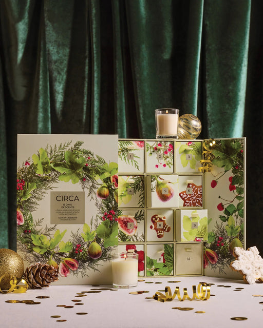 a Christmas-themed advent calendar with a wreath design, candles, and other holiday decorations arranged on a table.