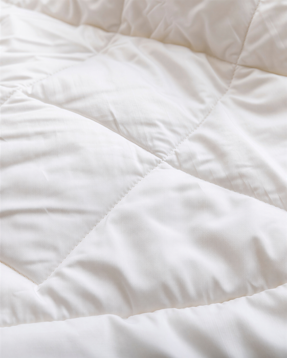 A close-up view of a white, fluffy fabric, possibly a blanket or comforter, with a slightly wrinkled texture.