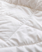 A close-up view of a white, fluffy fabric, possibly a blanket or comforter, with a slightly wrinkled texture.