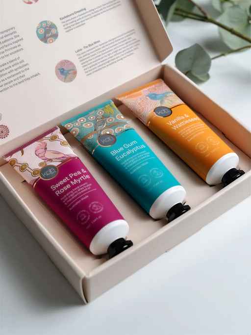 A set of three colorful hand cream tubes in a white box, with a natural background of greenery.