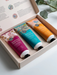 A set of three colorful hand cream tubes in a white box, with a natural background of greenery.