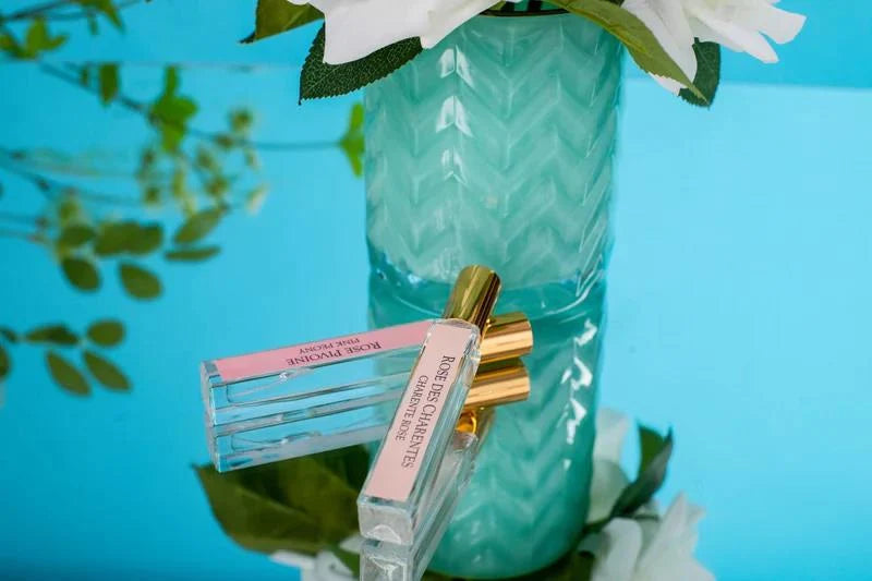 a vase with white flowers and a bottle of perfume placed on a blue surface.