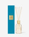 A tall blue box with a gold label and a clear glass bottle with white reeds inside, both placed against a white background.