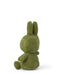 A green stuffed bunny toy is sitting on its back with its arms and legs spread out.