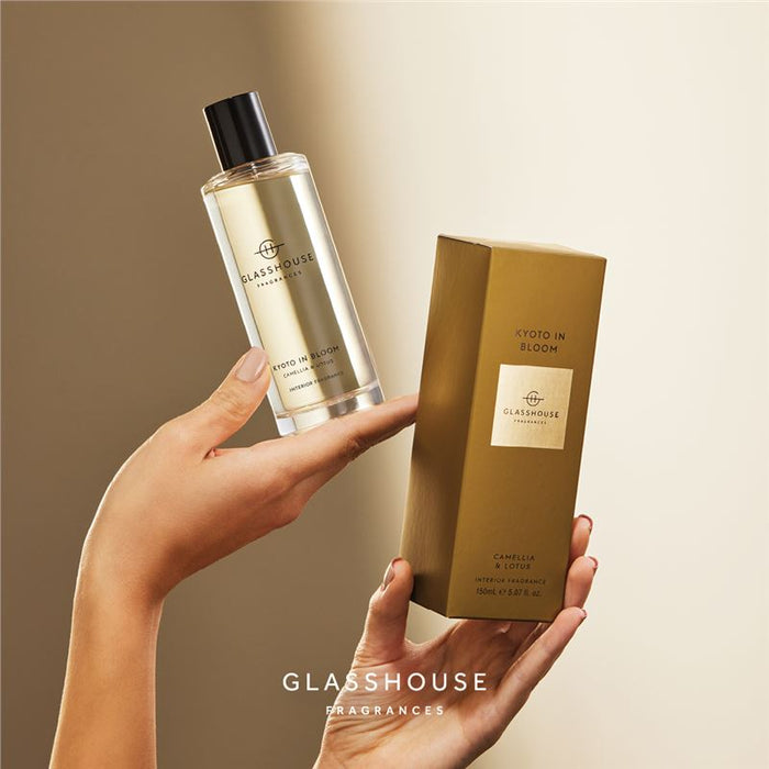 A person's hand holding a bottle of KYOTO IN BLOOM Fragrance by Glasshouse, along with its box, against a beige background.