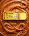 a yellow tin of Lucamar lip balm surrounded by caramel sauce and sprinkled with sea salt.