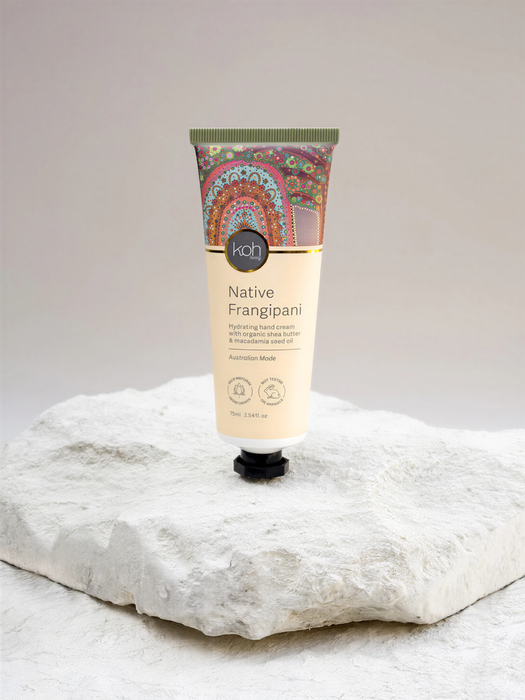A tube of "Koh" Native Frangipani hand cream with macadamia seed oil is displayed on a white rock.