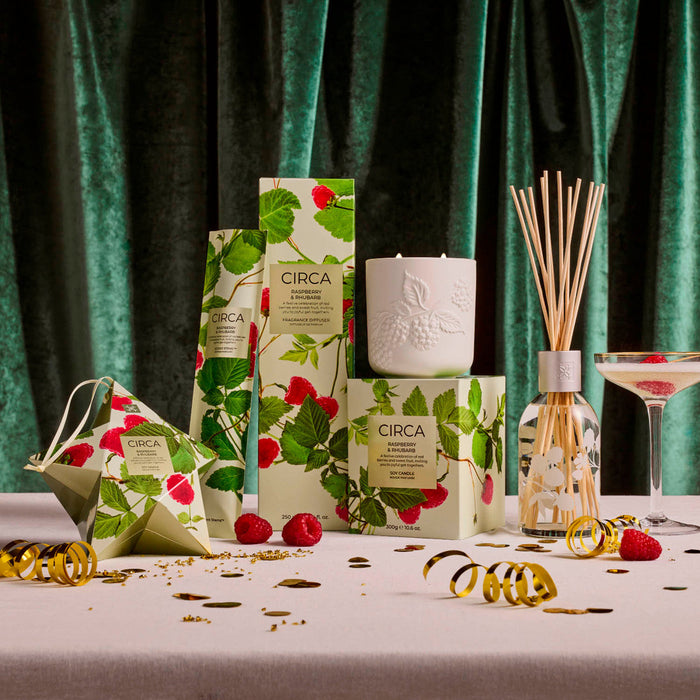 a collection of products with a focus on a white candle and a glass diffuser, surrounded by decorative elements such as a glass of wine, a ribbon, and a ribbon.