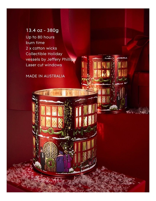 a red candle holder with a winter scene design, placed on a red surface with snow around it.