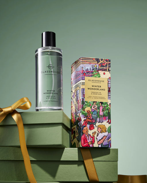 A bottle of "Winter Wonderland" eau de toilette and a box of "Glashouse Winter Wonderland" scented candles are displayed on a stack of green gift boxes against a green background.