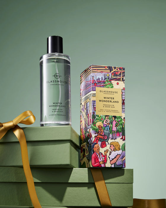 A bottle of "Winter Wonderland" eau de toilette and a box of "Glashouse Winter Wonderland" scented candles are displayed on a stack of green gift boxes against a green background.