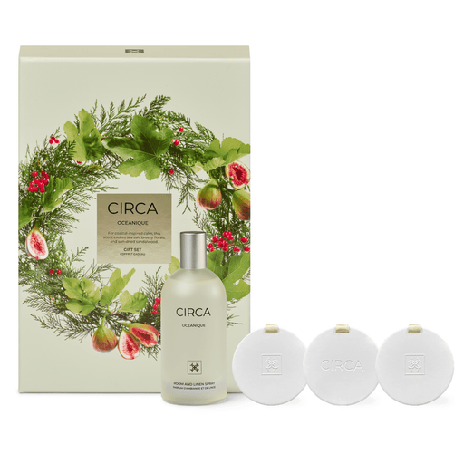 a set of three circular products with the word "CIRCA" on them, along with a bottle of "CIRCA" fragrance. The products are arranged in a row, with the bottle in the center and the other two products placed to the right. The background of the image is a wreath with greenery and red berries, creating a festive and holiday-themed setting.