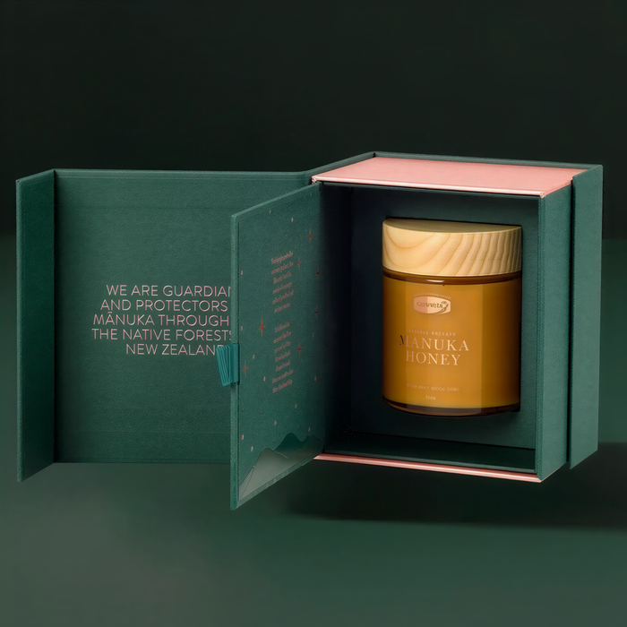 A jar of Manuka honey is displayed in a green box with a pink interior, set against a dark background.