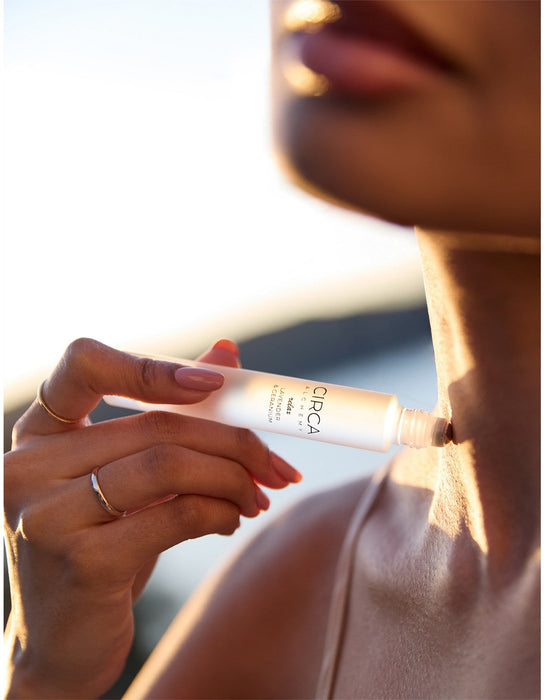 A close-up of a person's face holding a tube of product, with a blurred background suggesting a natural setting.