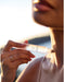 A close-up of a person's face holding a tube of product, with a blurred background suggesting a natural setting.