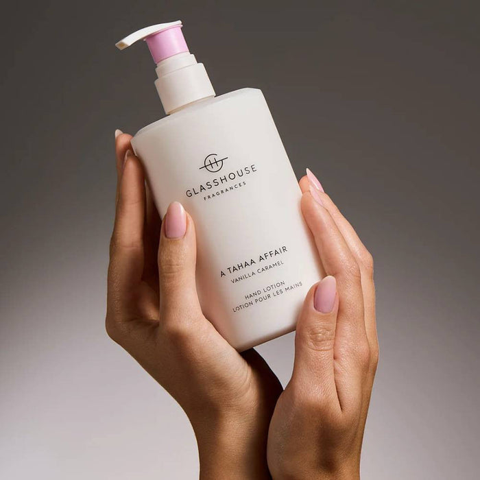 A hand holding a bottle of GLASSHOUSE Fragrance A.T.M.A.A.F.R. Vanilla Caramel Hand Lotion.