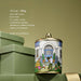 A decorative tin can with a house illustration and people, placed on a green surface.
