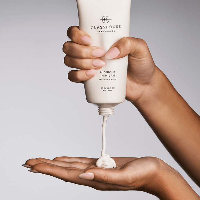 A person's hand is applying a body lotion from a tube, with the tube tilted upwards.