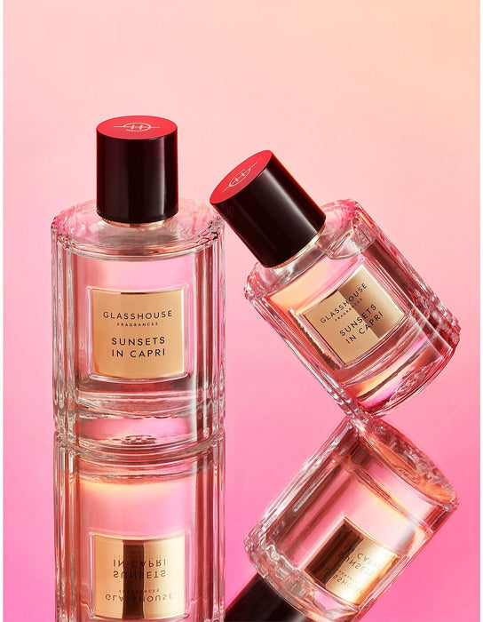 Two perfume bottles with red caps, labeled "GLASSHOUSE SUNSETS IN CAPRI", are displayed against a pink background.