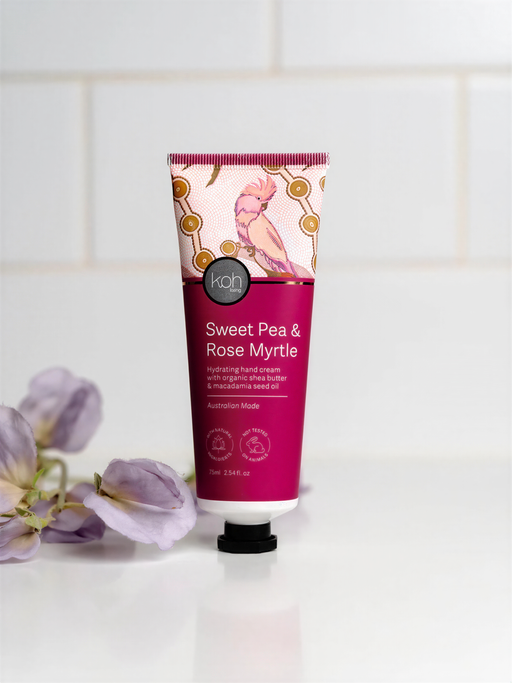 A tube of Sweet Pea & Rose Myrtle hand cream is displayed on a white countertop, with purple flowers in the background.