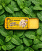 A yellow tin with a picture of a lamb and the text "My lips are sealed" is placed on top of a bed of green mint leaves.
