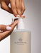 A person's hands are shown applying lotion from a transparent bottle with a pump dispenser, which is labeled "GLASSHOUSE Fragrances".