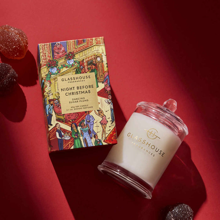 a box of Glashouse Fragrances Night Before Christmas Sugar Plums and a candle in a glass jar, both placed on a red surface.